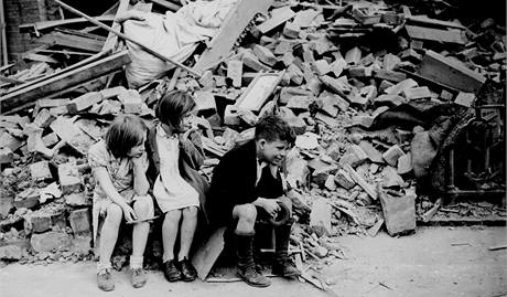 Děti z východního předměstí Londýna sedí u vybombardovaných trosek domu, kde předtím bydleli. (1940) Děti z východního předměstí Londýna sedí u vybombardovaných trosek domu, kde předtím bydleli. (1940)
